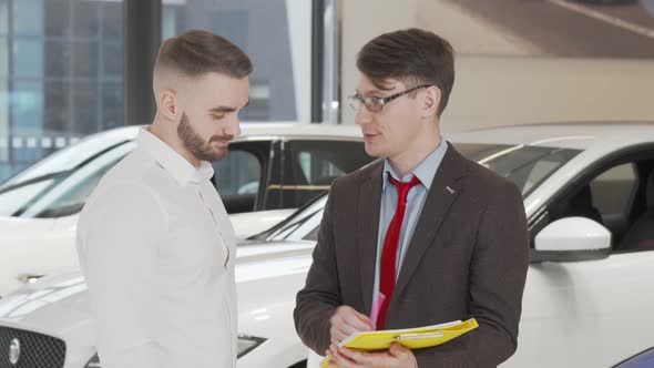 Handsome Man Signing Papers at Dealership After Buying New Automobile alt