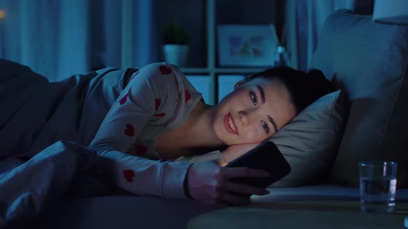 Teenage Girl in Pajamas with Phone in Bed at Night alt
