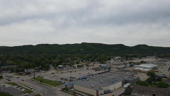 Aerial view of business area at edge of city in valley with mountains and gray cloudy sky.