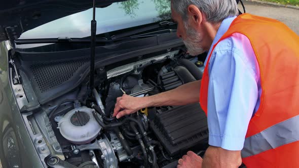 Senior Man Wears Warning Vest and Controls Engine of the Car - Closeup alt