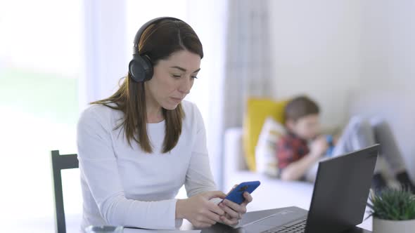 Mother working from home with son sitting in background alt
