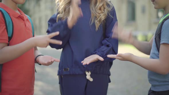 Unrecognizable Schoolchildren Playing Rock-paper-scissors Outdoors. Three Positive Caucasian Pupils alt