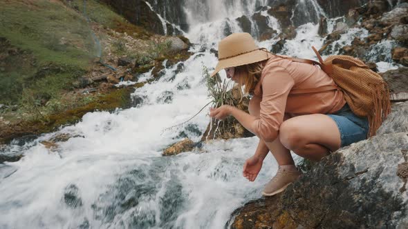 A Tourist Picks Up and Drinks Water From a Mountain River alt
