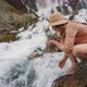 A Tourist Picks Up and Drinks Water From a Mountain River - VideoHive Item for Sale