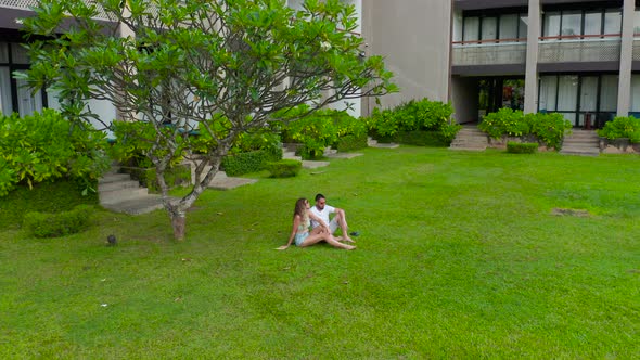 Couple Man and Woman Seat on the Grass Against the Trees in the Tropics Resort in SriLanka alt