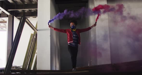 Mixed race man holding blue and purple flares walking through an empty building alt