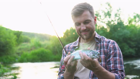 Fisherman Rests on the River and Catches Trout Smiles and Shows the Fish in the Camera alt