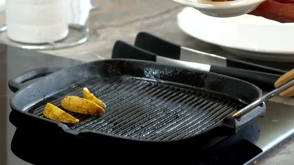 Chef Puts Potato Wedges in Black Frying Pan. Smoke Rises From Heated Skillet