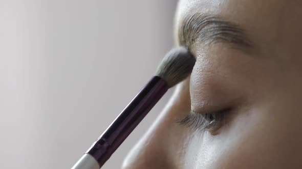 Visagist Is Applying Eye Shadows To Upper Eyelid of Young Model Eye Closeup