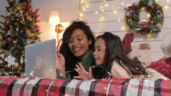 Joyful Mom and Daughter Communicate By Video Call with a Laptop at Home While Lying on the Bed alt