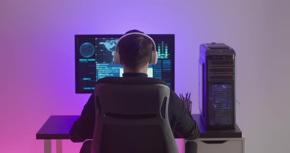 Man Programmer in Headphones Happy with Success While Working at a Computer in Data Center at Night alt
