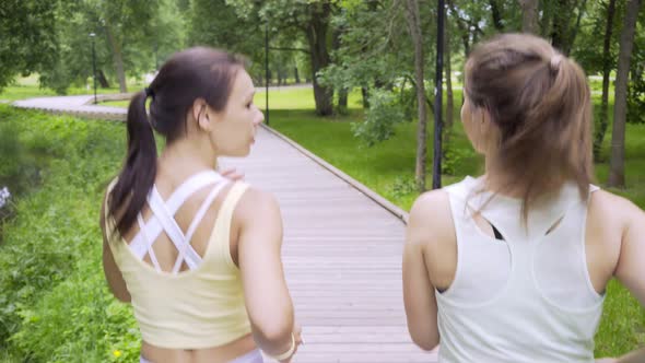 Strong Slim Girls Run Along Wooden Track in Public Garden
