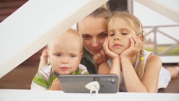 Two Little Children and Their Smiling Blond Mom Looking at Photos in Smartphone