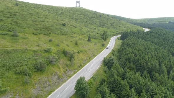 Aerial View of White Camper Caravan or Cargo Van Driving on Mountain Highway Against Beautiful Green alt