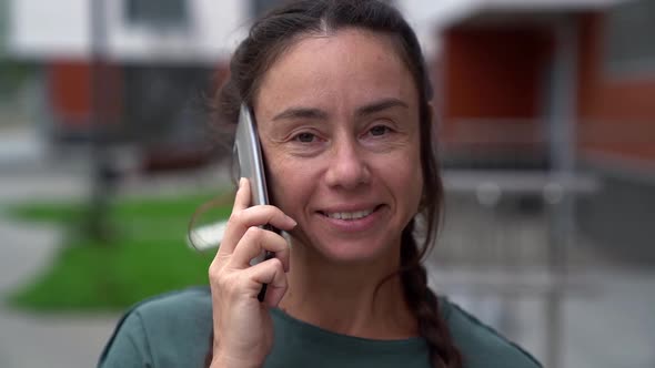 Close Up of an Adult Woman Smiling Talking on a Smartphone Against the Background of a Modern alt