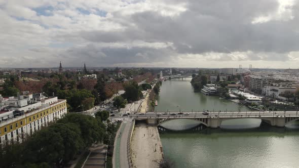 Aerial pullback Guadalquivir river bridge reveal Gold Tower on riverside, Seville