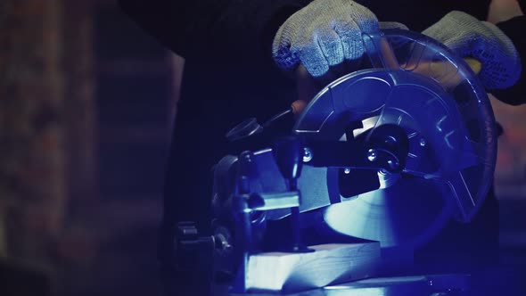 Worker Carpenter Sawing Board with a Circular End Saw in His Carpentry Workshop alt