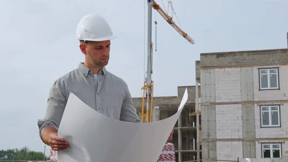 An Architect in a Hard Hat Managing a Project Standing with Drawings on a Construction Site alt