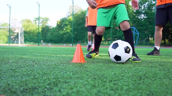 Boy in Football Uniform Training with Ball Around Small Racks to Improve His Speed During Workout alt