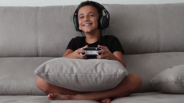 Boy Smiling and Having Fun Playing a Video Game with Controllers on a Couch