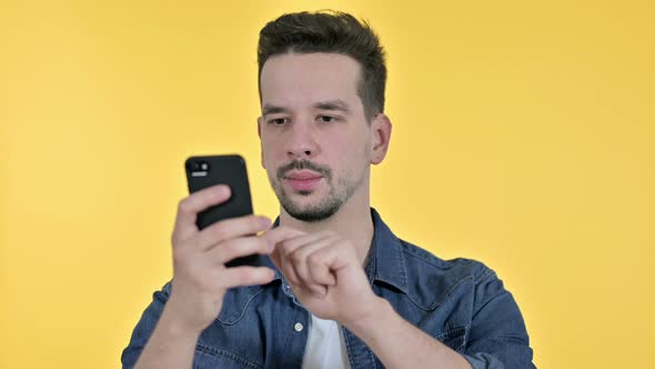 Portrait of Attractive Young Man Using Smartphone, Yellow Background alt