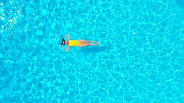 View From the Top As a Woman in a Yellow Swimsuit Lying on Her Back in the Pool alt