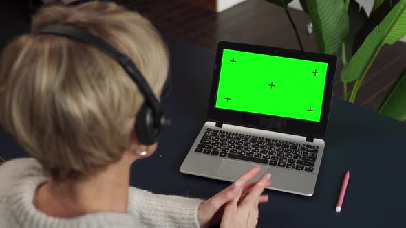 View Over the Shoulder of a Middleaged Woman in a Headset Working or Studying on a Laptop Computer alt