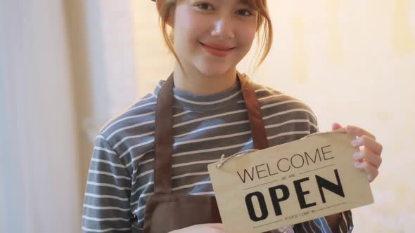 Business owner attractive young Asian woman in apron hanging we're open alt