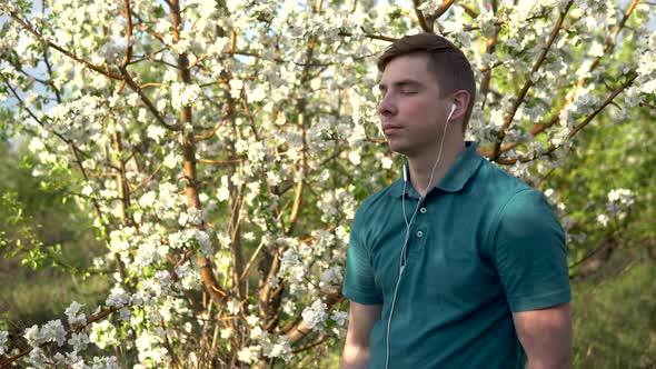 Young Man in Nature with Headphones in His Ears. A Man Listens To Music While Standing Against a alt
