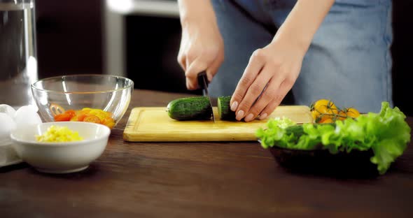 Women's Hands Cut a Cucumber with a Knife on a Cutting Board