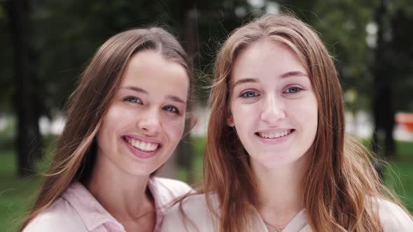 Pretty smiling girls students look at camera and smiling. Close up portrait of happy sisters. alt