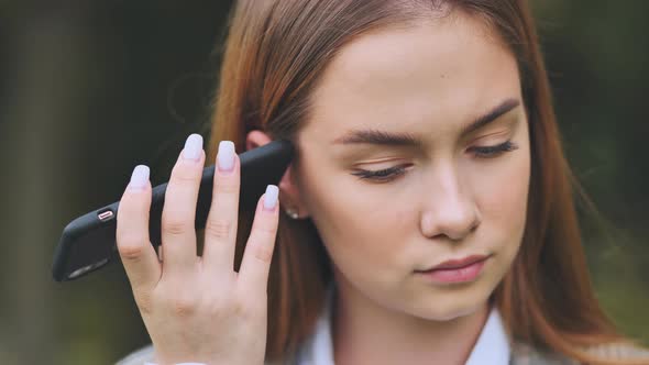 A Young Beautiful Girl Listens to an Audio Message on Her Phone alt