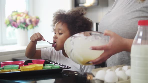 Family Baking  Black Little Girl and Her Mother Pouring Liquid Dough in Small Cake Moulds alt