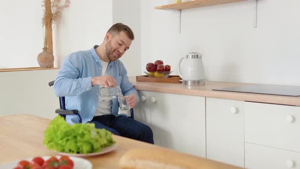 Joyful Disabled Person in a Wheelchair Pours Water Into a Glass in the Kitchen alt