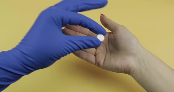 Doctor Hand Dressed in Blue Medical Glove Puts One White Pill Into Woman Hand alt