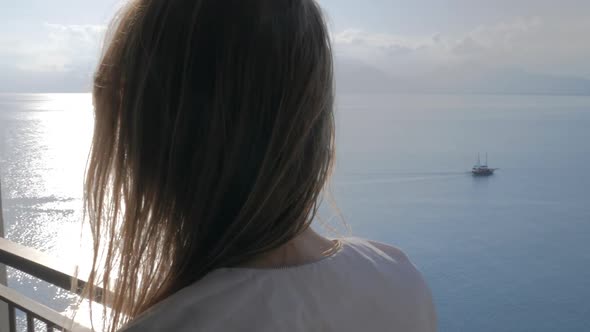 A Woman on a Balcony Talking To a Phone and a Sea View Behind Her alt