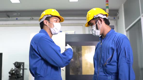 Asian male worker in safety uniform wearing protective mask giving high five with colleague