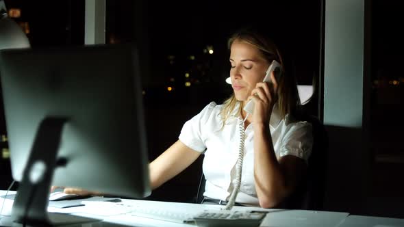 Businesswoman working over computer while talking on the phone alt