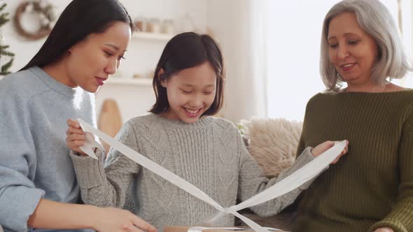 Cheerful Asian Girl Opening Christmas Gift with Mother and Grandma alt