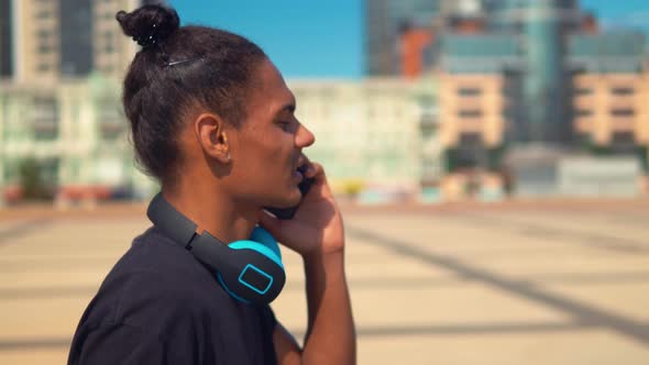 Side View Hipster Guy with Earphones Has Phone Conversation Walks in Town alt