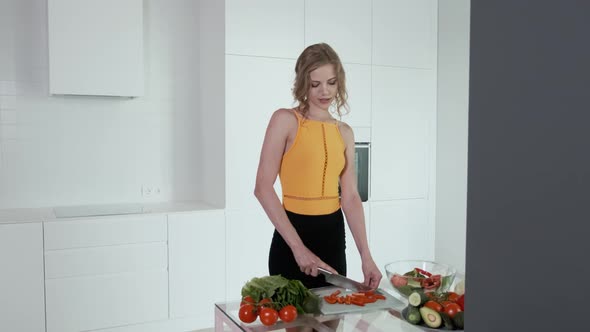 Young Woman Slicing Red Pepper For Vegetable Salad.  White Modern Kitchen.