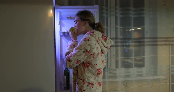 Young Woman Opens the Refrigerator at Night and Takes Food