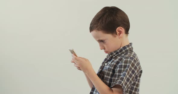 Young boy plays with a mobile phone on a white studio background alt