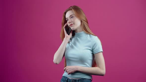 The Happy Freckled Young Woman Receives a Call and Speaks Enthusiastically on the Phone in a Pink alt