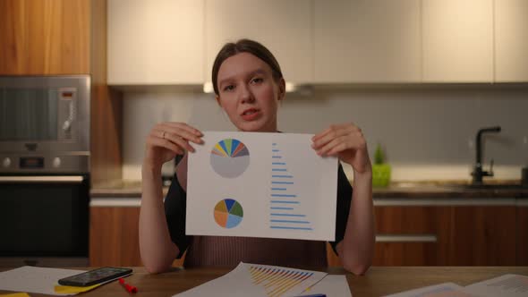 Home Office Looking at the Camera A Young Woman Shows a Graph in a Laptop Camera Sitting at Home in alt