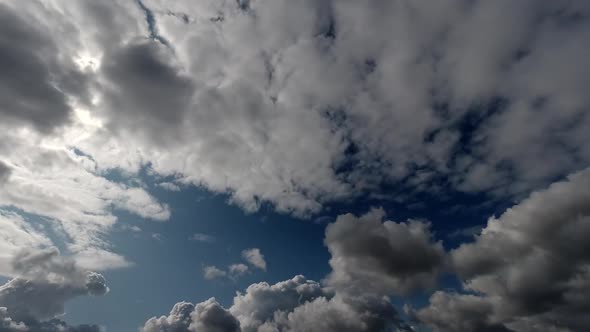 Time lapse: the sun hidden behind fluffy clouds flying in the sky. alt