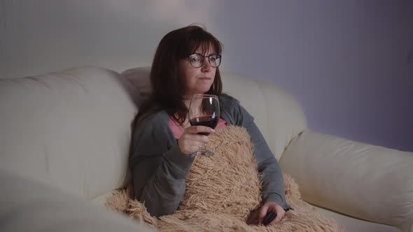 Brunette Woman Relax at Home with a Glass of Wine on the Sofa and Watches Tv in the Evening
