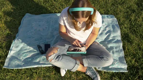 Top View of Young Female with Gadgets and Headphones in the Park on Green Grass alt