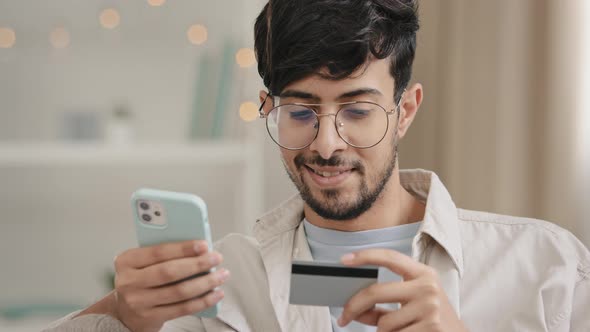Closeup Bearded Arabic Business Man in Glasses with Credit Card and Phone Makes Purchase Online alt