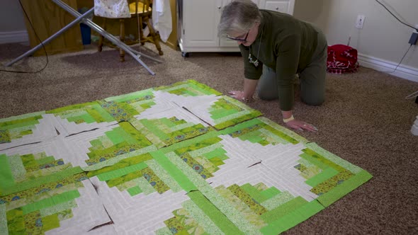 A senior Caucasian woman completes the final arrangement of her quilt blocks alt